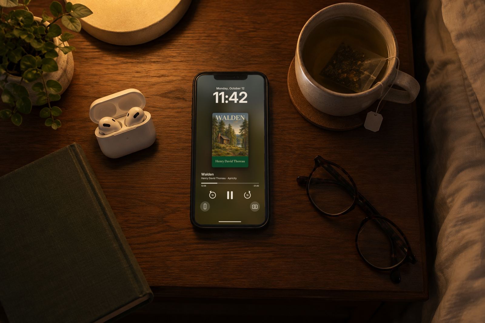 An iPhone on a bedside table at night, its Lock Screen playing Walden, beside AirPods, glasses and a cup of tea